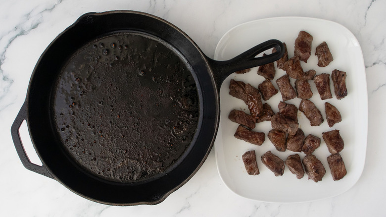 Empty skillet next to plate with steak bites