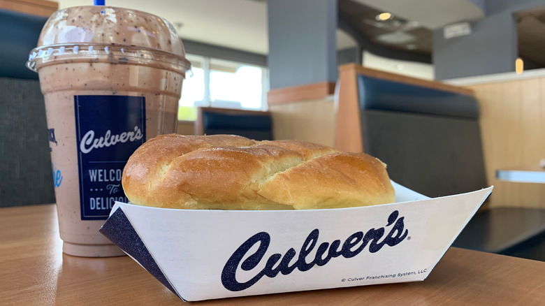 Milkshake and cardboard basket with the bun of a sandwich peaking out on a table inside of a Culver's.