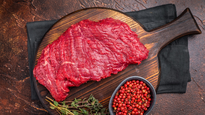 Raw beef sirloin flap steak on a wooden cutting board next to herbs