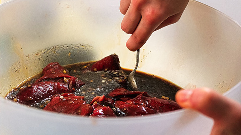 Slices of beef marinating in a dark liquid as a person stirs them with a metal spoon