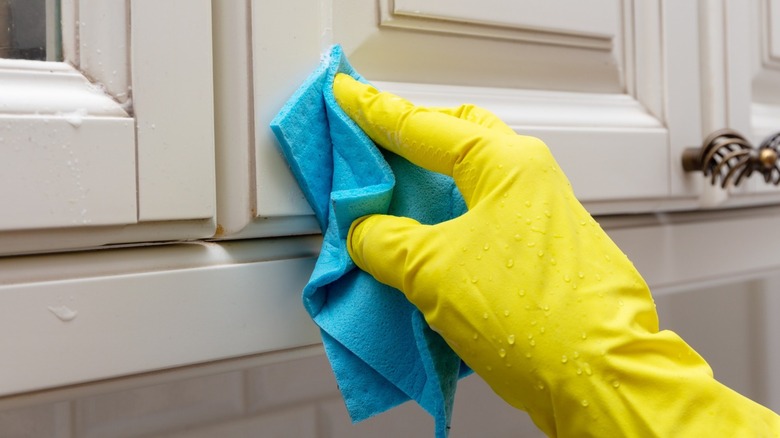 Hand wearing rubber glove cleaning cabinet