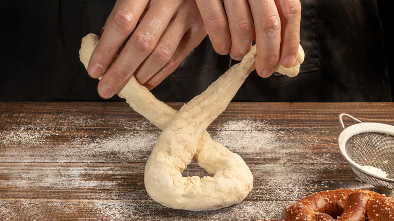 person folding a soft pretzel on a wooden board