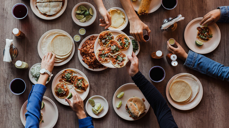 People preparing tacos on wooden table 