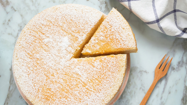 A rounded vainilla cake with icing next to a fork