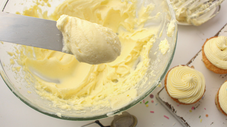 bowl of cream cheese frosting with spreader and cupcakes