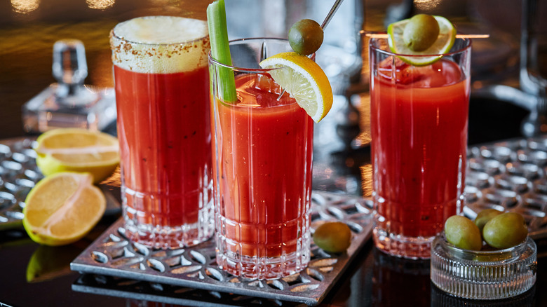 Three glasses of Bloody Mary cocktails garnished with olives, lemons, and celery