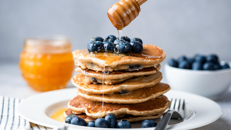 A stack of pancakes topped with blueberries and honey