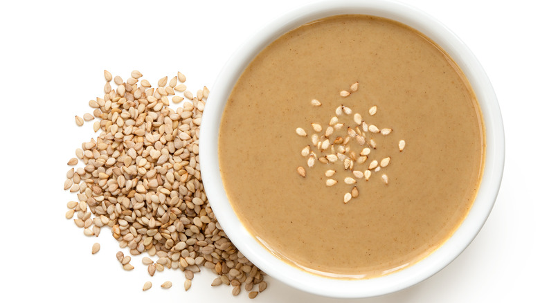 Tahini in a small white ceramic bowl with sesame seeds on top 