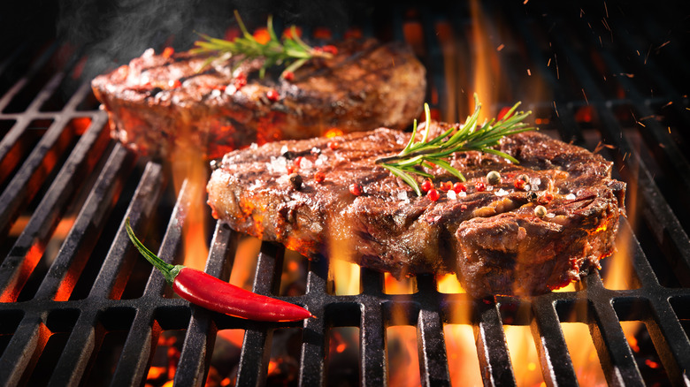 Two steaks over fire grill with pepper