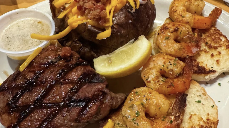A plate of food from Texas Roadhouse, including: a steak, shrimp, and a loaded mashed potato