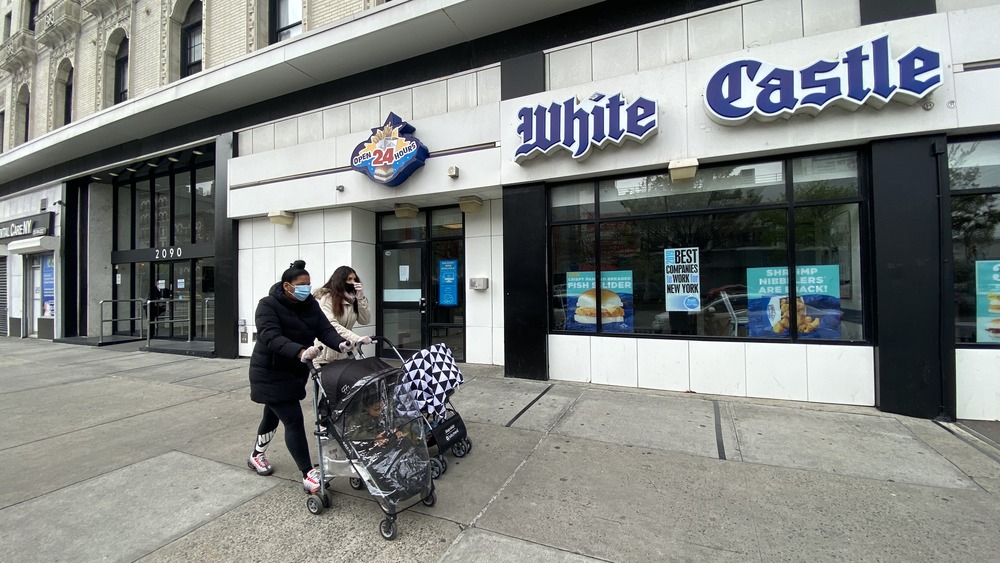 People wearing face masks walk in front of a White Castle