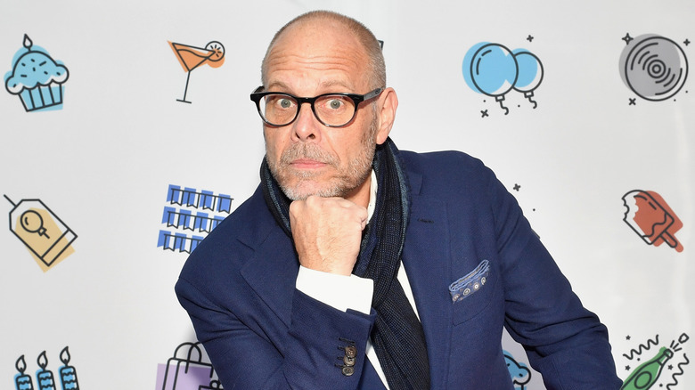 Alton Brown, chin on fist, wearing a blue suit