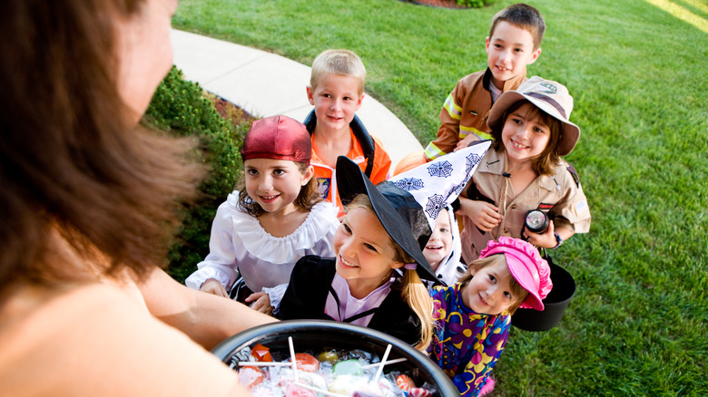 a woman handing out halloween candy to trick-or-treaters wearing costumes