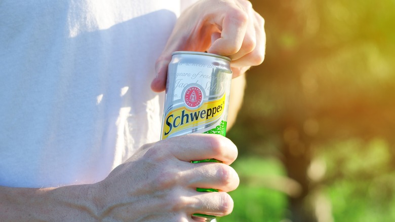 Person opening can of Schweppes