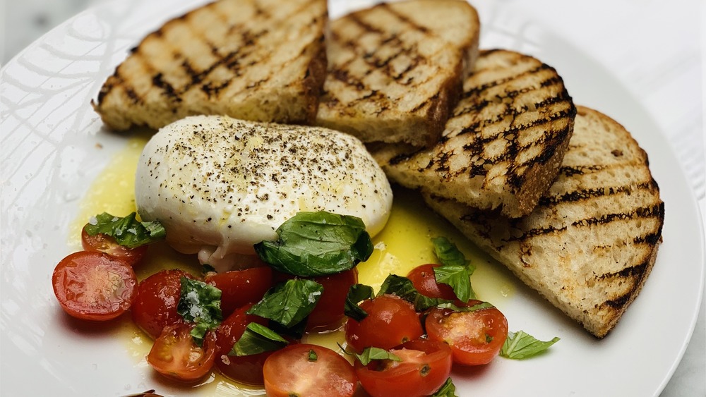 burrata cheese on white place with tomatoes and grilled bread