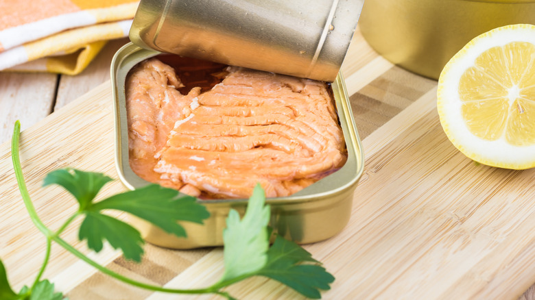 opened can of salmon on wooden cutting board 