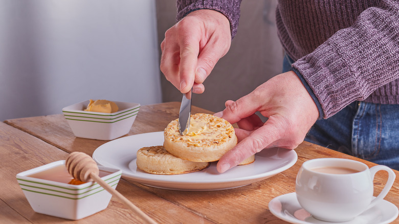 hand buttering crumpet with mug of tea