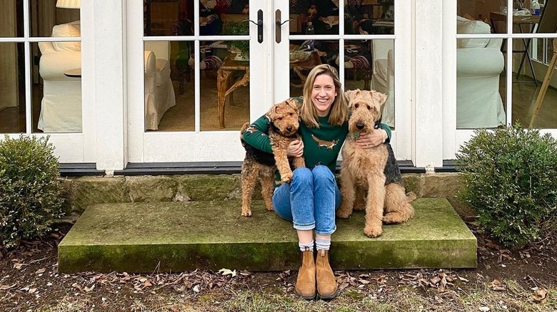 Lidey Heuck sitting on grassy stoop between two dogs