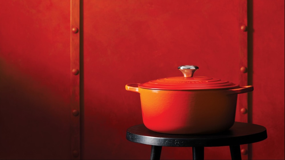 Le Creuset dutch oven in classic "flame" color set against a red-orange background.