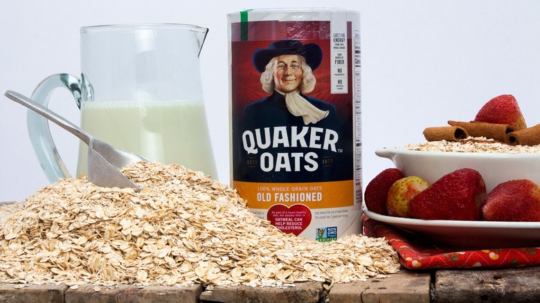 Quaker Oats container with pile of loose oats, pitcher of milk, dish with strawberries and cinnamon sticks