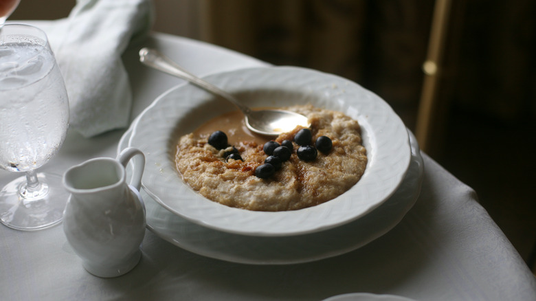 Dish of oatmeal and berries on white tablecloth with spoon and water glass