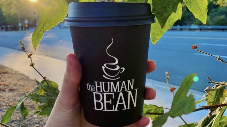 Hand holding The Human Bean coffee cup