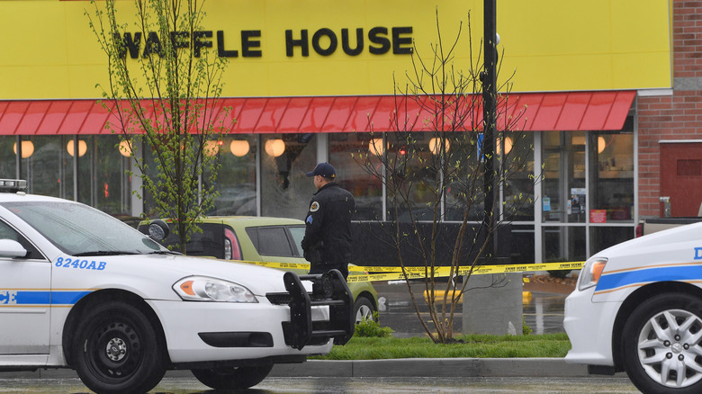 The exterior of a Waffle House with yellow caution tape and a police officer out front