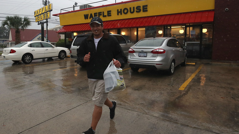A man walking with a bag of food outside Waffle House