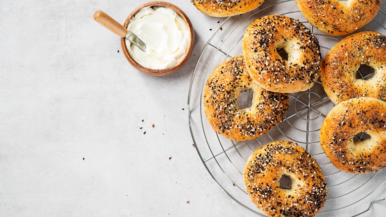 Multiple bagels on a wire rack with a bowl of cream cheese