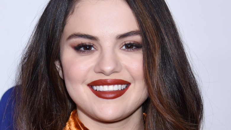 Selena Gomez wearing red lipstick and smiling while posing at an event.