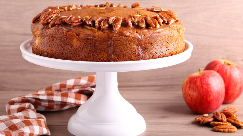 Apple cider cake on cake stand with apples and pecans