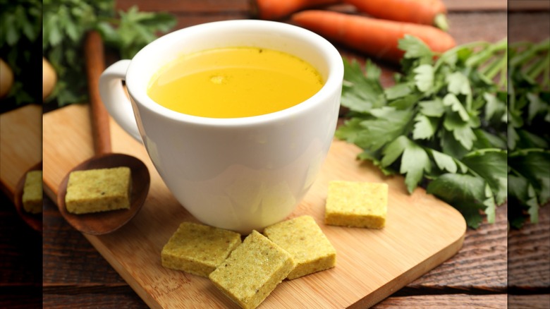 cup of broth on cutting board surrounded by bouillon cubes