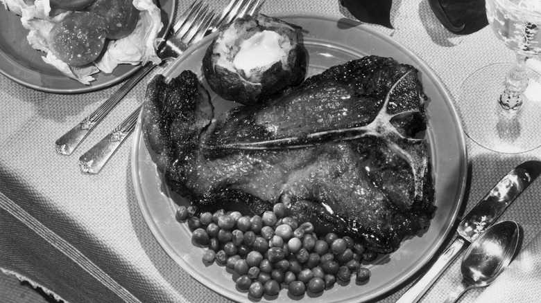 Black and white photo of a t-bone steak with peas.