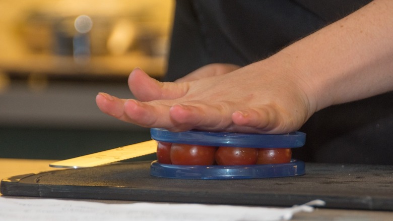 Person slicing cherry tomatoes with plastic lids