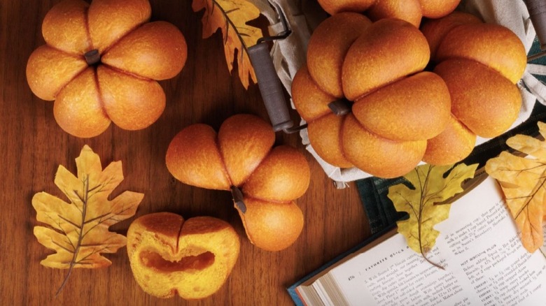 Pumpkin-shaped pumpkin bread on a wooden table in cloth-covered basket next to fall leaves and book