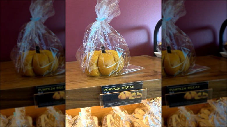 A single cellophane bag with a pumpkin-shaped pastry on a wooden shelf with a price label beneath it