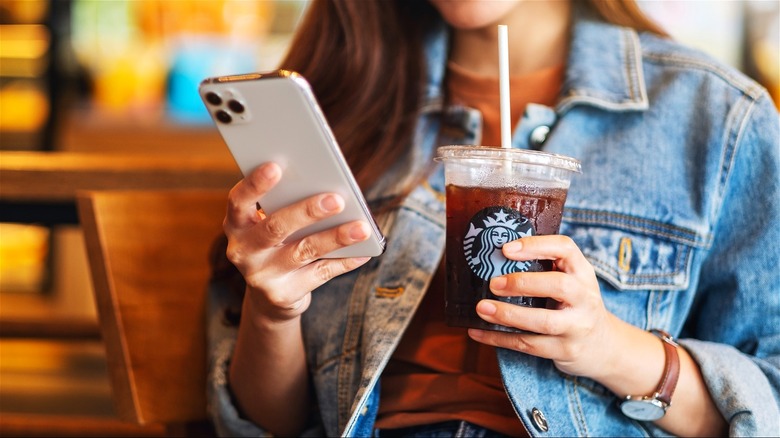 Woman looking at Iphone holding an iced Starbucks beverage