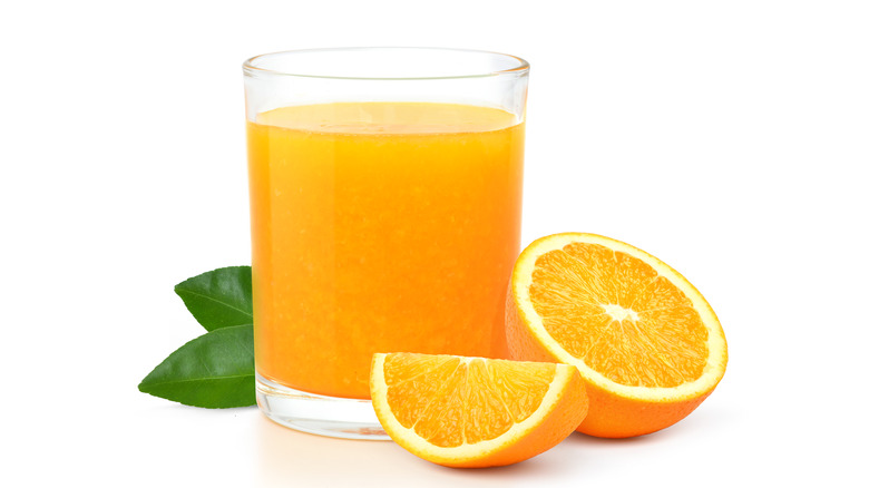 Sliced orange next to glass of orange juice on white background