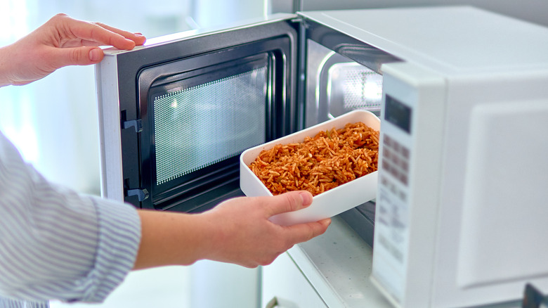 person putting dish in microwave