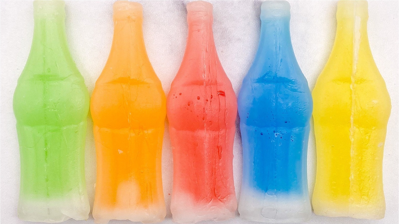 a group of 5 wax bottle candies, with colored liquid inside. They are green, orange, red, blue, and yellow.