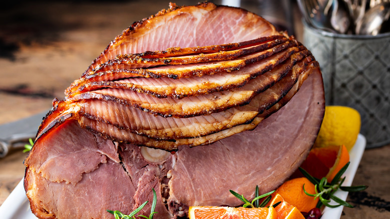 A spiral cut ham garnished with rosemary sprigs and orange wedges