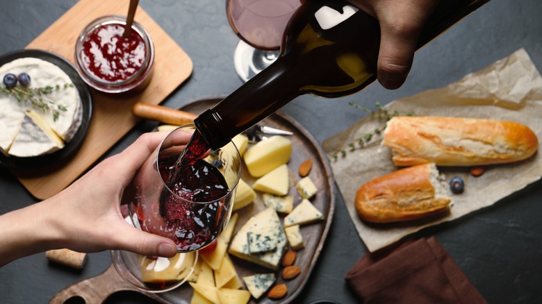 pouring wine into glass over a cheese board