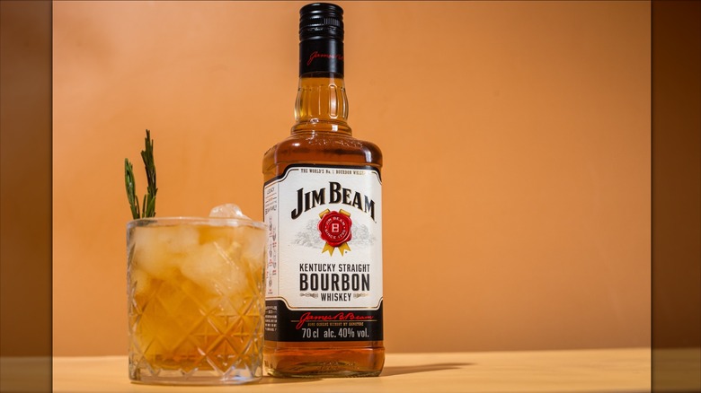 Rocks glass with whiskey and garnish beside a Jim Beam bottle