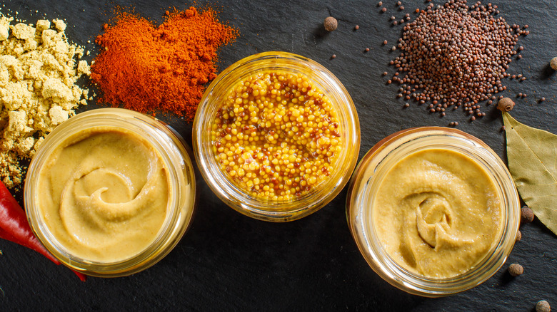 A trio of mustards in jars, surrounded by spices