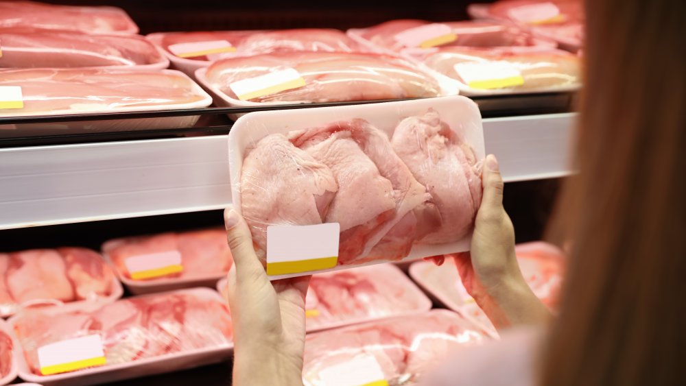 Woman choosing between cuts of chicken in grocery store aisle