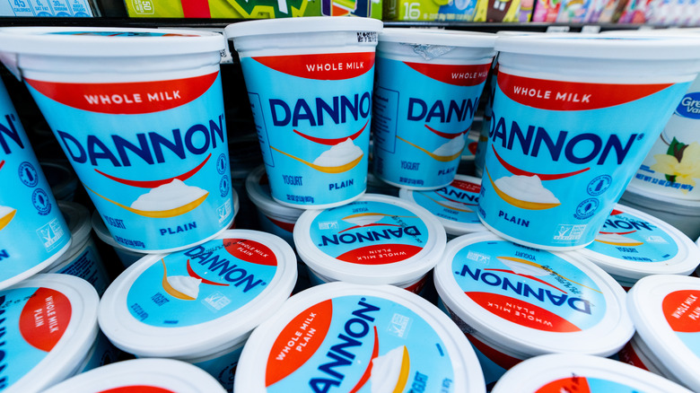 Stack of Dannon plain whole milk yogurt tubs in grocery store.