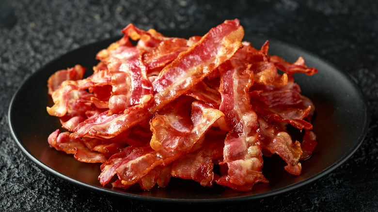 A stack of crispy bacon on a black plate with black background