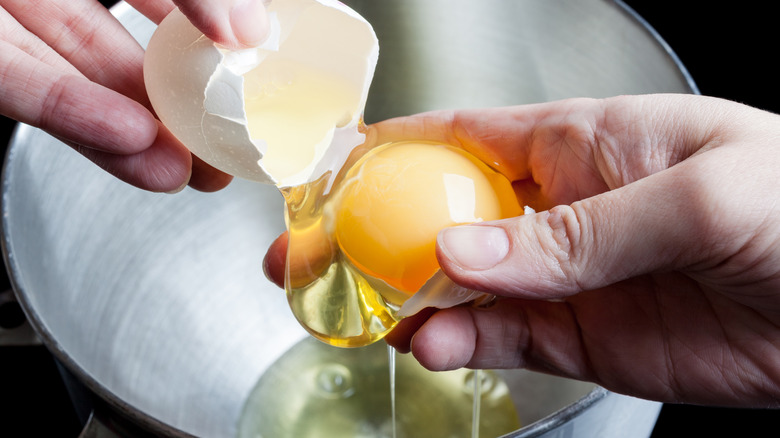An egg being cracked into a metal bowl.