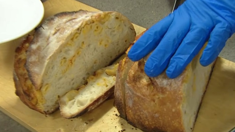Gloved hand cutting slices of mac and cheese sourdough bread