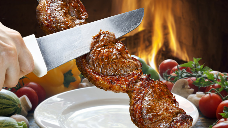 person cutting through Brazilian barbecue skewers with large knife